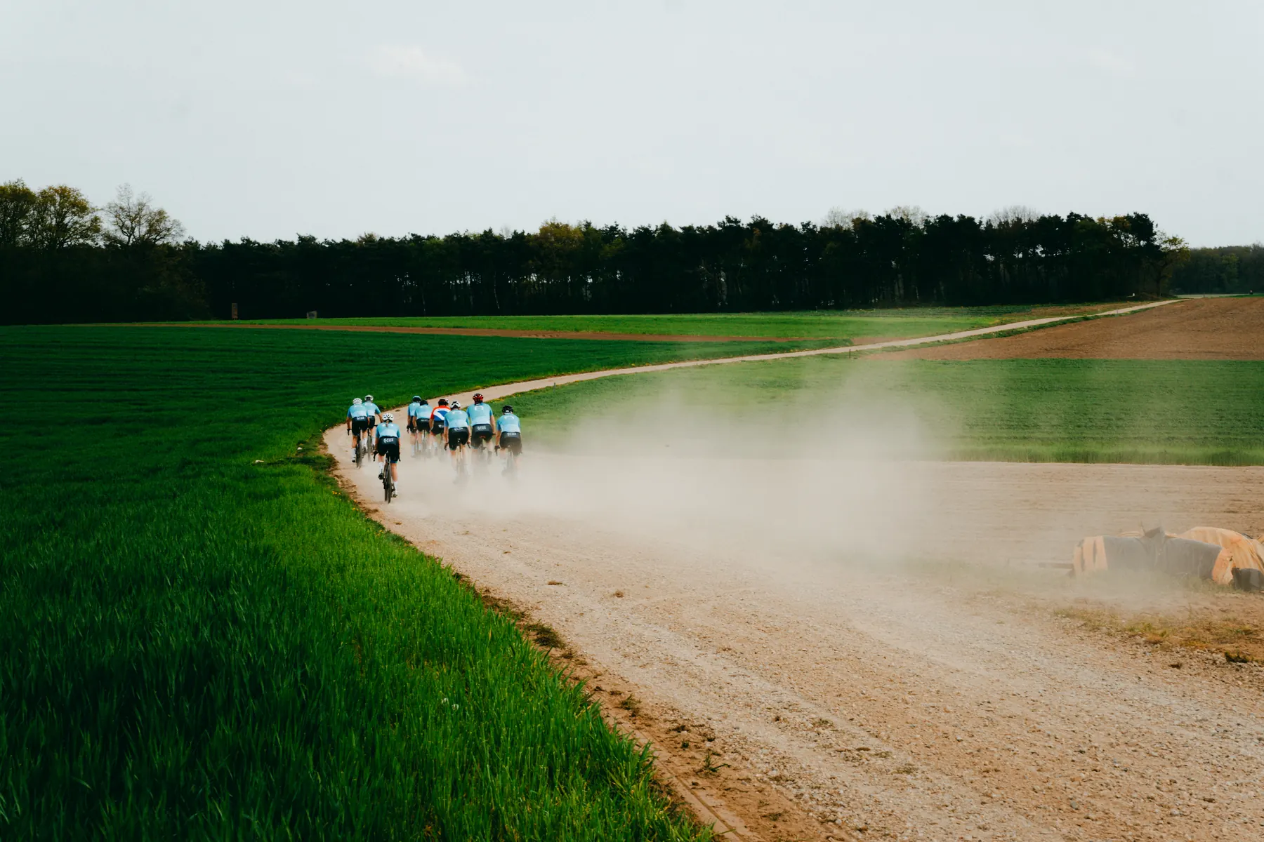 Groep Ride2Connect-fietsers rijdt over een stoffig gravelpad tussen de velden